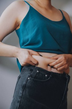 Şişman kadın, şişko, obez kadın el ele tutuşan ölçü bandıyla göbek yağı, kadın diyeti yaşam tarzı konsepti