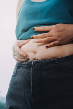 Şişman kadın, şişko, obez kadın el ele tutuşan ölçü bandıyla göbek yağı, kadın diyeti yaşam tarzı konsepti