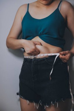 Şişman kadın, şişko, obez kadın el ele tutuşan ölçü bandıyla göbek yağı, kadın diyeti yaşam tarzı konsepti