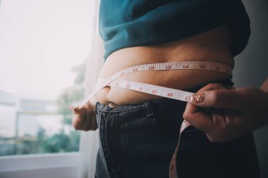 Şişman kadın, şişko, obez kadın el ele tutuşan ölçü bandıyla göbek yağı, kadın diyeti yaşam tarzı konsepti