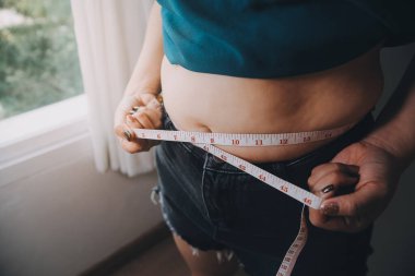 Şişman kadın, şişko, obez kadın el ele tutuşan ölçü bandıyla göbek yağı, kadın diyeti yaşam tarzı konsepti