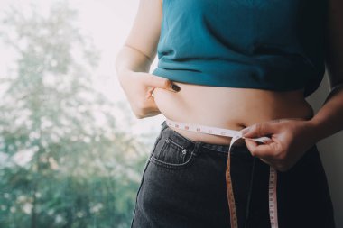 Şişman kadın, şişko, obez kadın el ele tutuşan ölçü bandıyla göbek yağı, kadın diyeti yaşam tarzı konsepti