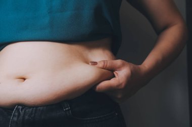 Şişman kadın, şişko, obez kadın el ele tutuşan ölçü bandıyla göbek yağı, kadın diyeti yaşam tarzı konsepti