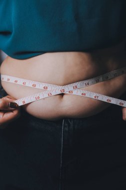 Şişman kadın, şişko, obez kadın el ele tutuşan ölçü bandıyla göbek yağı, kadın diyeti yaşam tarzı konsepti