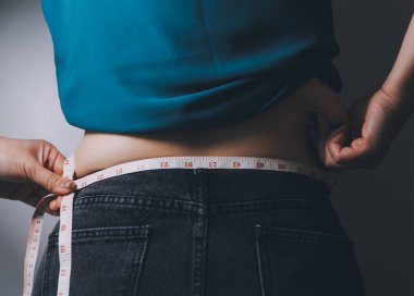 Şişman kadın, şişko, obez kadın el ele tutuşan ölçü bandıyla göbek yağı, kadın diyeti yaşam tarzı konsepti