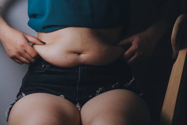 Şişman kadın, şişko, obez kadın el ele tutuşan ölçü bandıyla göbek yağı, kadın diyeti yaşam tarzı konsepti