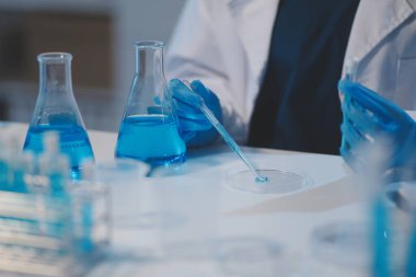 Kendini adamış bir grup bilim adamı tıbbi laboratuvarda kimyasal deney yapıyor. Aşı ilacı veya antibiyotik geliştirmek için pipetten deney tüpüne kesin miktarda sıvı döküyorlar. Neoterik
