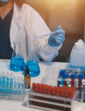 Kendini adamış bir grup bilim adamı tıbbi laboratuvarda kimyasal deney yapıyor. Aşı ilacı veya antibiyotik geliştirmek için pipetten deney tüpüne kesin miktarda sıvı döküyorlar. Neoterik