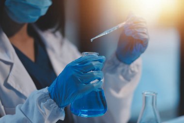 Kendini adamış bir grup bilim adamı tıbbi laboratuvarda kimyasal deney yapıyor. Aşı ilacı veya antibiyotik geliştirmek için pipetten deney tüpüne kesin miktarda sıvı döküyorlar. Neoterik