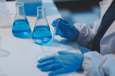 Kendini adamış bir grup bilim adamı tıbbi laboratuvarda kimyasal deney yapıyor. Aşı ilacı veya antibiyotik geliştirmek için pipetten deney tüpüne kesin miktarda sıvı döküyorlar. Neoterik