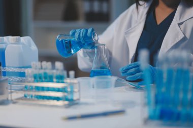 Kendini adamış bir grup bilim adamı tıbbi laboratuvarda kimyasal deney yapıyor. Aşı ilacı veya antibiyotik geliştirmek için pipetten deney tüpüne kesin miktarda sıvı döküyorlar. Neoterik