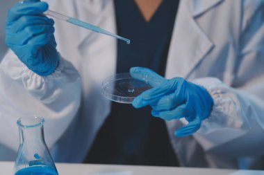 Kendini adamış bir grup bilim adamı tıbbi laboratuvarda kimyasal deney yapıyor. Aşı ilacı veya antibiyotik geliştirmek için pipetten deney tüpüne kesin miktarda sıvı döküyorlar. Neoterik