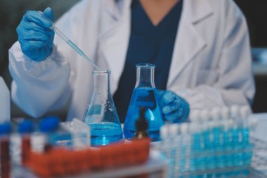 Kendini adamış bir grup bilim adamı tıbbi laboratuvarda kimyasal deney yapıyor. Aşı ilacı veya antibiyotik geliştirmek için pipetten deney tüpüne kesin miktarda sıvı döküyorlar. Neoterik