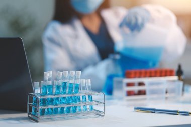 Kendini adamış bir grup bilim adamı tıbbi laboratuvarda kimyasal deney yapıyor. Aşı ilacı veya antibiyotik geliştirmek için pipetten deney tüpüne kesin miktarda sıvı döküyorlar. Neoterik