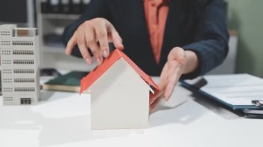 Arka planda ev modeli olan iş adamı el ele tutuşuyor. Emlak kavramı.