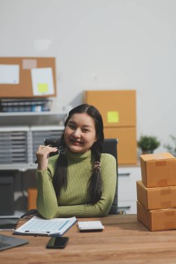 Girişim KOBİ küçük işletme girişimcisi önlük giyen Asyalı kadın dizüstü bilgisayar ve kutu kullanarak çevrimiçi müşterilere, çevrimiçi sme iş fikirlerine satış hazırlamak için siparişleri alır ve gözden geçirir.