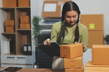Girişim KOBİ küçük işletme girişimcisi önlük giyen Asyalı kadın dizüstü bilgisayar ve kutu kullanarak çevrimiçi müşterilere, çevrimiçi sme iş fikirlerine satış hazırlamak için siparişleri alır ve gözden geçirir.