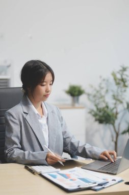 Başarılı Asyalı iş kadını dizüstü bilgisayarla gülümseyip ofisinde kahve fincanı tutuyor. Güvenilir Asyalı iş kadını ofiste mutlu mesut oturuyor..