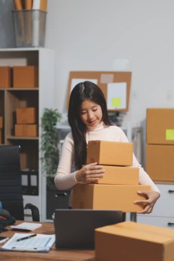 Girişim KOBİ küçük işletme girişimcisi önlük giyen Asyalı kadın dizüstü bilgisayar ve kutu kullanarak çevrimiçi müşterilere, çevrimiçi sme iş fikirlerine satış hazırlamak için siparişleri alır ve gözden geçirir.