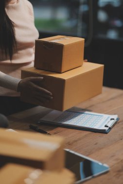 Girişim KOBİ küçük işletme girişimcisi önlük giyen Asyalı kadın dizüstü bilgisayar ve kutu kullanarak çevrimiçi müşterilere, çevrimiçi sme iş fikirlerine satış hazırlamak için siparişleri alır ve gözden geçirir.