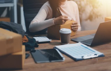 Girişim KOBİ küçük işletme girişimcisi önlük giyen Asyalı kadın dizüstü bilgisayar ve kutu kullanarak çevrimiçi müşterilere, çevrimiçi sme iş fikirlerine satış hazırlamak için siparişleri alır ve gözden geçirir.