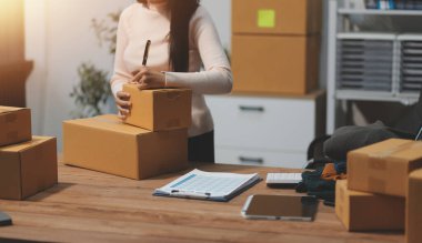 Girişim KOBİ küçük işletme girişimcisi önlük giyen Asyalı kadın dizüstü bilgisayar ve kutu kullanarak çevrimiçi müşterilere, çevrimiçi sme iş fikirlerine satış hazırlamak için siparişleri alır ve gözden geçirir.