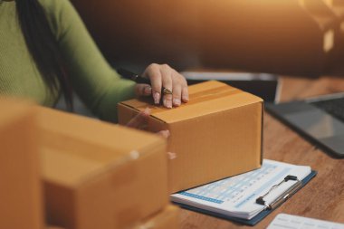 Girişim KOBİ küçük işletme girişimcisi önlük giyen Asyalı kadın dizüstü bilgisayar ve kutu kullanarak çevrimiçi müşterilere, çevrimiçi sme iş fikirlerine satış hazırlamak için siparişleri alır ve gözden geçirir.