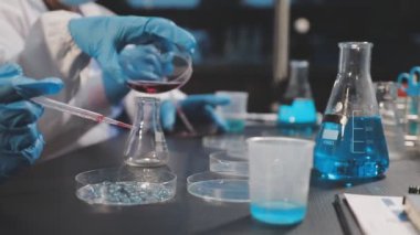 Koruyucu eldivenli kadın bilim adamı laboratuarda kimyasal deneyler yapıyor.