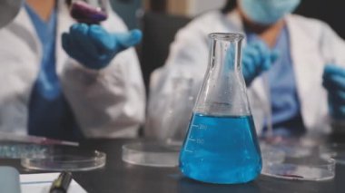 Laboratuvar asistanı elinde kimyasal numuneyle mavi matara tutuyor, yakın plan.