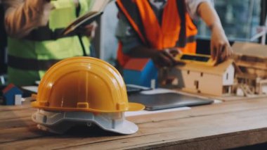 İnşaat alanında mühendis veya işçi veya miğfer veya güvenlik şapkası güvenlik yeleği, cetvel veya arka plandaki ahşap masada kalem.