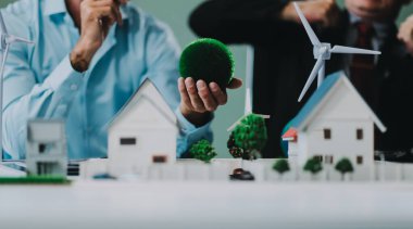 Rüzgar türbini modeli ve ev modeli için mühendisler buluşuyor. Yenilenebilir enerji ve konut geliştirme kavramı. Modern ofiste mimarlardan ve mühendislerden oluşan bir ekip tasarım yapısını tartışıyor..