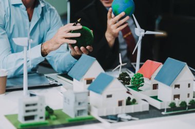 Rüzgar türbini modeli ve ev modeli için mühendisler buluşuyor. Yenilenebilir enerji ve konut geliştirme kavramı. Modern ofiste mimarlardan ve mühendislerden oluşan bir ekip tasarım yapısını tartışıyor..