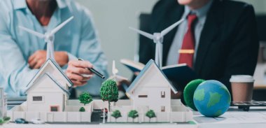 Rüzgar türbini modeli ve ev modeli için mühendisler buluşuyor. Yenilenebilir enerji ve konut geliştirme kavramı. Modern ofiste mimarlardan ve mühendislerden oluşan bir ekip tasarım yapısını tartışıyor..