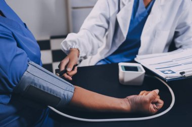 Hastanın tansiyonunu ölçen bir doktor. Hastanın kolunda tansiyon aleti var. Doktor da tansiyon monitörü kullanıyor..