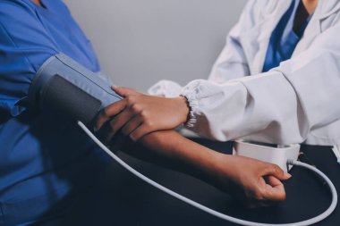 Hastanın tansiyonunu ölçen bir doktor. Hastanın kolunda tansiyon aleti var. Doktor da tansiyon monitörü kullanıyor..