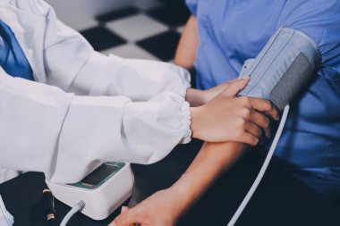 Hastanın tansiyonunu ölçen bir doktor. Hastanın kolunda tansiyon aleti var. Doktor da tansiyon monitörü kullanıyor..