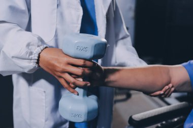 Evde dambıl kullanarak fizyoterapist eğitimi alan yaşlı bir kadın. Terapist, huzurevi egzersizlerinde yaşlı kadına yardım ediyor. Yaşlı bir hasta kollarını uzatmış halterler kullanıyor..