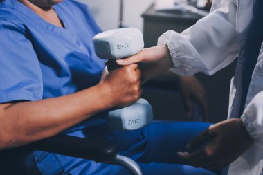 Evde dambıl kullanarak fizyoterapist eğitimi alan yaşlı bir kadın. Terapist, huzurevi egzersizlerinde yaşlı kadına yardım ediyor. Yaşlı bir hasta kollarını uzatmış halterler kullanıyor..