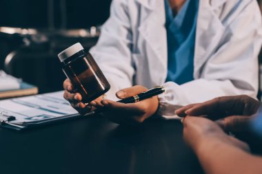 Evde dizüstü bilgisayar kullanan yaşlı kadın hemşireyle birlikte ilaç şişesini tutuyor.