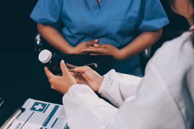 Evde dizüstü bilgisayar kullanan yaşlı kadın hemşireyle birlikte ilaç şişesini tutuyor.