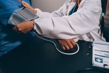 Hastanın tansiyonunu ölçen bir doktor. Hastanın kolunda tansiyon aleti var. Doktor da tansiyon monitörü kullanıyor..