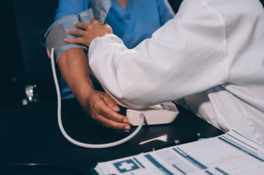 Hastanın tansiyonunu ölçen bir doktor. Hastanın kolunda tansiyon aleti var. Doktor da tansiyon monitörü kullanıyor..