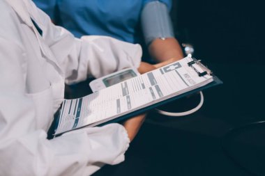 Hastanın tansiyonunu ölçen bir doktor. Hastanın kolunda tansiyon aleti var. Doktor da tansiyon monitörü kullanıyor..