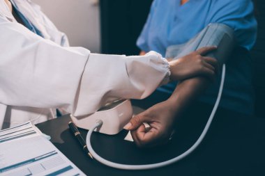 Hastanın tansiyonunu ölçen bir doktor. Hastanın kolunda tansiyon aleti var. Doktor da tansiyon monitörü kullanıyor..