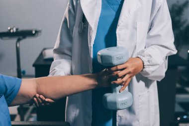 Evde dambıl kullanarak fizyoterapist eğitimi alan yaşlı bir kadın. Terapist, huzurevi egzersizlerinde yaşlı kadına yardım ediyor. Yaşlı bir hasta kollarını uzatmış halterler kullanıyor..