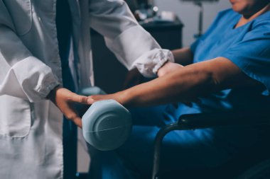 Evde dambıl kullanarak fizyoterapist eğitimi alan yaşlı bir kadın. Terapist, huzurevi egzersizlerinde yaşlı kadına yardım ediyor. Yaşlı bir hasta kollarını uzatmış halterler kullanıyor..