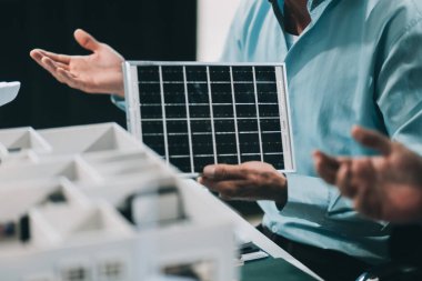 Rüzgar türbini modeli ve ev modeli için mühendisler buluşuyor. Yenilenebilir enerji ve konut geliştirme kavramı. Modern ofiste mimarlardan ve mühendislerden oluşan bir ekip tasarım yapısını tartışıyor..