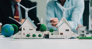 Rüzgar türbini modeli ve ev modeli için mühendisler buluşuyor. Yenilenebilir enerji ve konut geliştirme kavramı. Modern ofiste mimarlardan ve mühendislerden oluşan bir ekip tasarım yapısını tartışıyor..