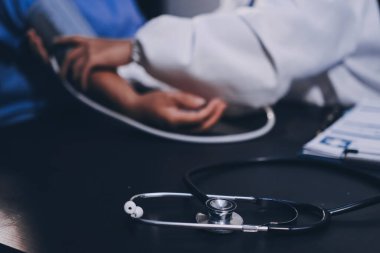 Hastanın tansiyonunu ölçen bir doktor. Hastanın kolunda tansiyon aleti var. Doktor da tansiyon monitörü kullanıyor..