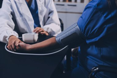 Hastanın tansiyonunu ölçen bir doktor. Hastanın kolunda tansiyon aleti var. Doktor da tansiyon monitörü kullanıyor..